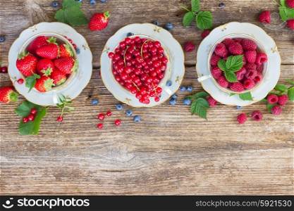 fresh raspberry , red currand and strawberry with green leaves in cups, top view