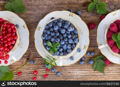 fresh raspberry, red currunt and blueberry with green leaves in cups, top view
