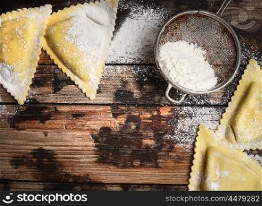 Fresh ravioli and flour on rustic wooden background, top view