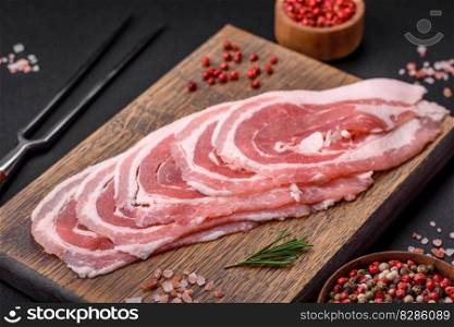 Fresh raw bacon sliced with spices and herbs on a dark concrete background