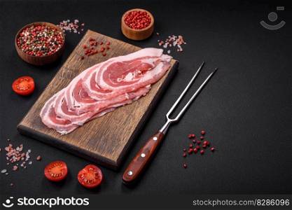 Fresh raw bacon sliced with spices and herbs on a dark concrete background