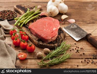 Fresh raw barbeque braising beef steak on chopping board with asparagus and garlic with cherry tomatoes and salt with pepper on wooden background with hatchet.