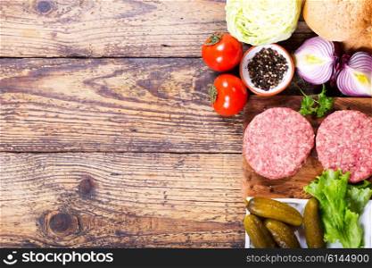Fresh raw beef burger for hamburger with vegetables on wooden board, top view