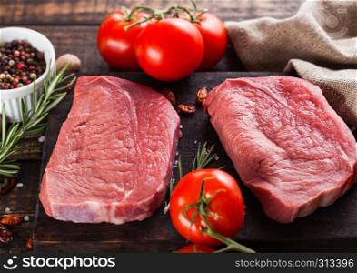 Fresh raw beef steak meat on wooden kitchen board with tomatoes and pepper
