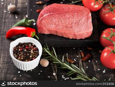 Fresh raw beef steak meat on wooden kitchen board with tomatoes and pepper