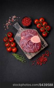 Fresh raw beef steak with bone or ossobuco with salt, spices and herbs on dark concrete background
