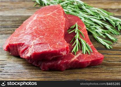 Fresh raw beef steak with rosemary on brown wooden table. Fresh raw meat with rosemary