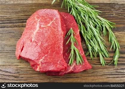 Fresh raw beef steak with rosemary on brown wooden table. Top view. Fresh raw meat with rosemary