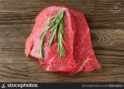Fresh raw beef steak with rosemary on brown wooden table. Top view. Fresh raw meat with rosemary on brown wooden background
