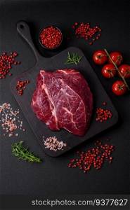 Fresh raw beef steak with salt, spices and herbs on a dark concrete background