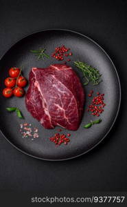 Fresh raw beef steak with salt, spices and herbs on a dark concrete background