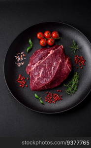Fresh raw beef steak with salt, spices and herbs on a dark concrete background