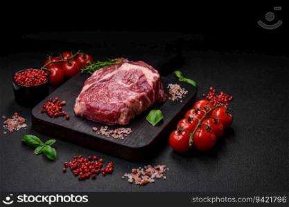 Fresh, raw beef steak with salt, spices and herbs on a dark textured background