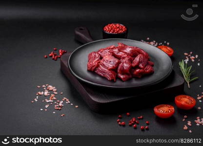 Fresh raw beef with salt, spices and herbs on a dark concrete background