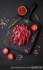 Fresh raw beef with salt, spices and herbs on a dark concrete background