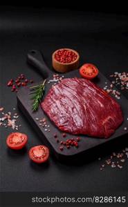 Fresh raw beef with salt, spices and herbs on a dark concrete background