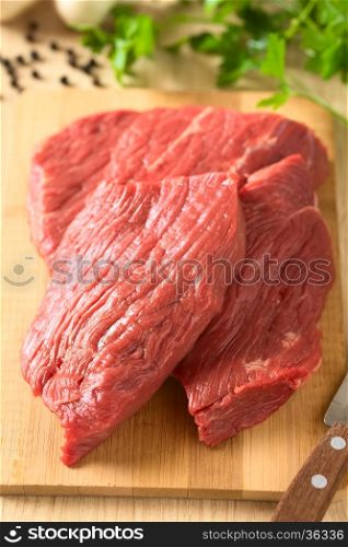 Fresh raw boneless beef meat cut in slices on wooden board, photographed with natural light (Selective Focus, Focus in the middle of the image)