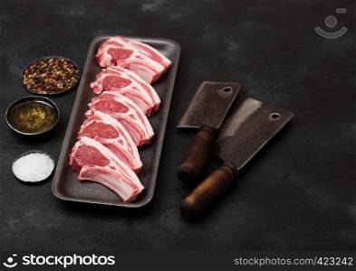Fresh raw butchers lamb beef cutlets in plastic tray with vintage meat hatchets on black background.Salt, pepper and oil