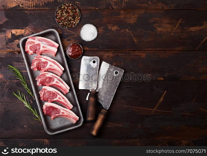 Fresh raw butchers lamb beef cutlets in plastic tray with vintage meat hatchets on wooden background.Salt, pepper and oil