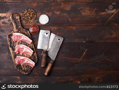 Fresh raw butchers lamb beef cutlets on chopping board with vintage meat hatchets on wooden background.Salt, pepper and oil