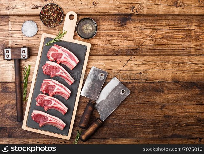 Fresh raw butchers lamb beef cutlets on chopping board with vintage meat hatchets and hammer on wooden background.Salt, pepper and oil