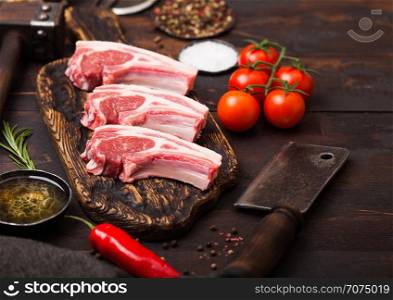 Fresh raw butchers lamb beef cutlets on chopping board with vintage meat hatchet and hammer on wooden background.Salt, pepper and oil with tomatoes and garlic and barbecue sauce
