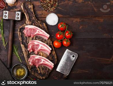 Fresh raw butchers lamb beef cutlets on chopping board with vintage meat hatchet and hammer on wooden background.Salt, pepper and oil with tomatoes and garlic and barbecue sauce