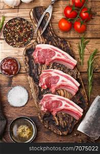 Fresh raw butchers lamb beef cutlets on chopping board with vintage meat hatchets on wooden background.Salt, pepper and oil with tomatoes and garlic and barbeque sauce.
