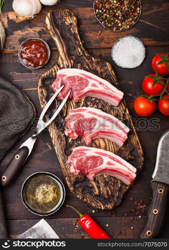 Fresh raw butchers lamb beef cutlets on chopping board with vintage meat fork and knife on wooden background.Salt, pepper and oil with tomatoes and garlic and barbecue sauce.