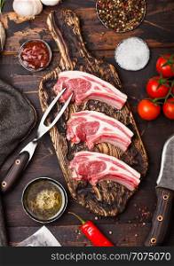 Fresh raw butchers lamb beef cutlets on chopping board with vintage meat fork and knife on wooden background.Salt, pepper and oil with tomatoes and garlic and barbecue sauce.