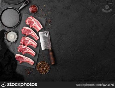 Fresh raw butchers lamb beef cutlets on stone board with vintage hatchet on black background.
