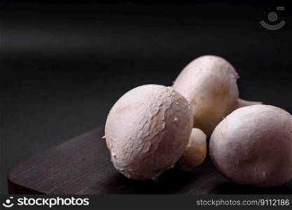 Fresh raw champignon mushrooms on a wooden cutting board with spices and herbs on a dark concrete background