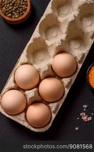 Fresh raw chicken eggs in beige color in a cardboard tray on a dark concrete background