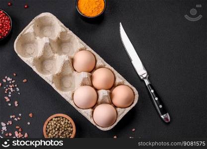 Fresh raw chicken eggs in beige color in a cardboard tray on a dark concrete background