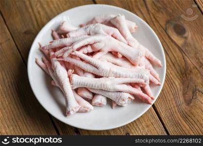 Fresh raw chicken feet for cooked food on the wooden table kitchen background, chicken feet on white plate