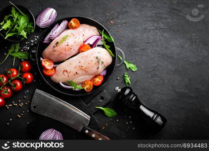 Fresh raw chicken meat, fillet marinated with spices, onion and tomatoes on black background. Top view