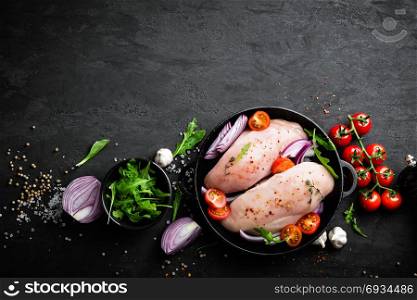 Fresh raw chicken meat, fillet marinated with spices, onion and tomatoes on black background. Top view