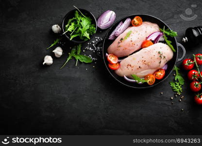 Fresh raw chicken meat, fillet marinated with spices, onion and tomatoes on black background. Top view