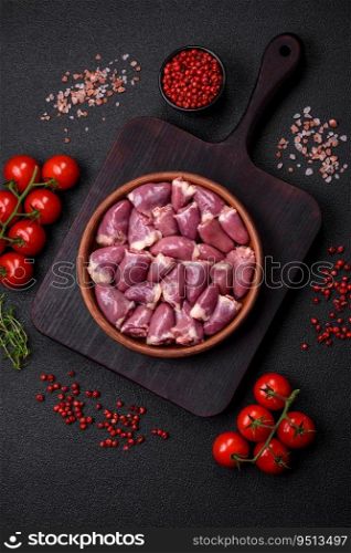 Fresh raw chicken or turkey hearts in a ceramic plate with salt, spices and herbs on a dark concrete background