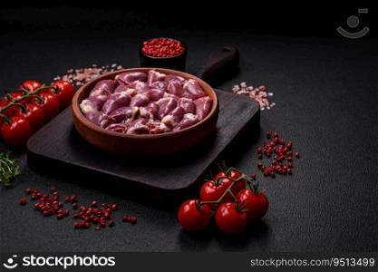 Fresh raw chicken or turkey hearts in a ceramic plate with salt, spices and herbs on a dark concrete background