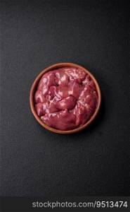 Fresh raw chicken or turkey liver in a ceramic plate with salt, spices and herbs on a dark concrete background