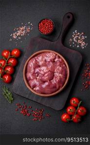 Fresh raw chicken or turkey liver in a ceramic plate with salt, spices and herbs on a dark concrete background