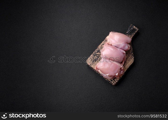 Fresh raw chicken thigh fillets with salt, spices and herbs on a dark concrete background