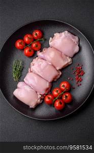 Fresh raw chicken thigh fillets with salt, spices and herbs on a dark concrete background