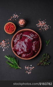 Fresh raw chicken, turkey or duck liver with salt, spices and herbs on a dark concrete background