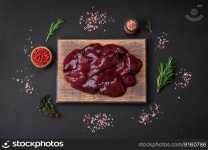 Fresh raw chicken, turkey or duck liver with salt, spices and herbs on a dark concrete background