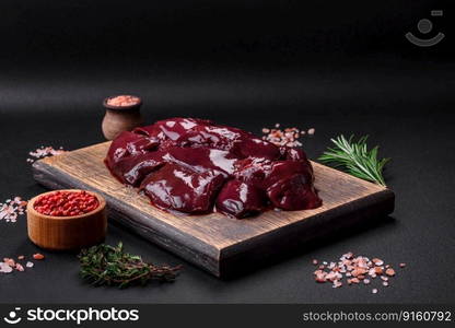 Fresh raw chicken, turkey or duck liver with salt, spices and herbs on a dark concrete background