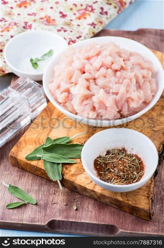 Fresh raw chopped chicken meat in a bowl with seasoning and sage, selective focus