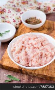 Fresh raw chopped chicken meat in a bowl with seasoning and sage, selective focus