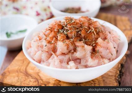 Fresh raw chopped chicken meat with seasoning in a bowl, closeup, selective focus